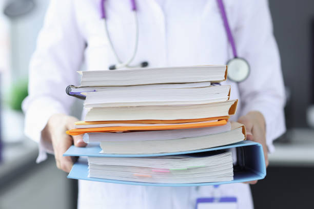 Doctor is holding large stack of folders Doctor is holding large stack of folders. Disease history concept exam paper stock pictures, royalty-free photos & images