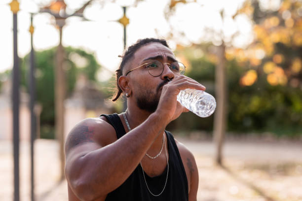 афро-американский мальчик-спортсмен с татуировкой пьет воду из бутылки в парке. - body building exercising one man only tattoo стоковые фото �и изображения