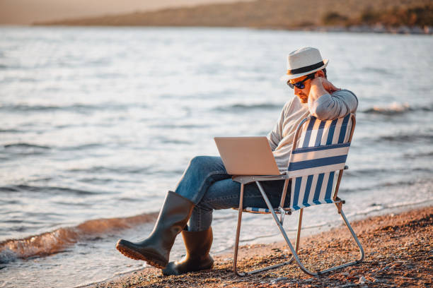 istock Freelance Young Man Working on Laptop on the Beach 1300463018
