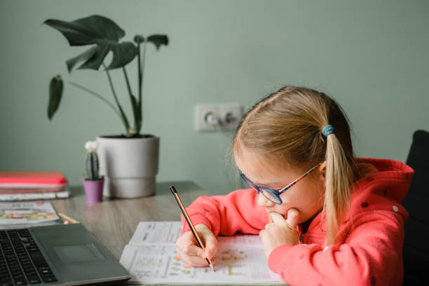istock Junior student girl in eyeglasses writing in her notebook while studying online 1300463850