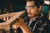 Carpenter man professional skilled in wood work looking detail of masterpiece woodcraft in furniture workshop