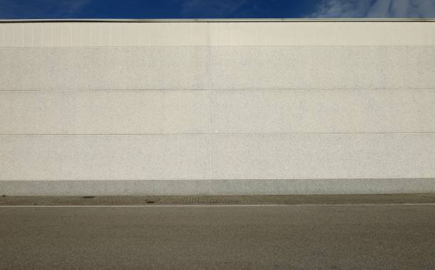 istock White concrete wall with horizontal blocks. Tiled sidewalk and asphalt road in front. 1300467413