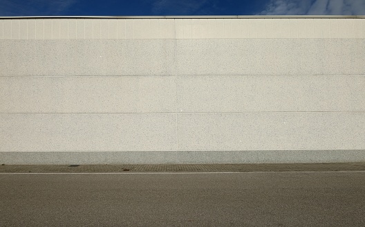 White concrete wall with horizontal blocks. Tiled sidewalk and asphalt road in front. Background for copy space