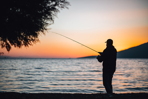 Young Man Fishing at the Beach at Sunset