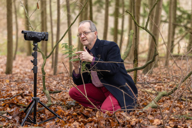 istock Middle aged man in forest vlogging about nature, ferns and environmental conservation for youtube or social media educational channels 1300469935