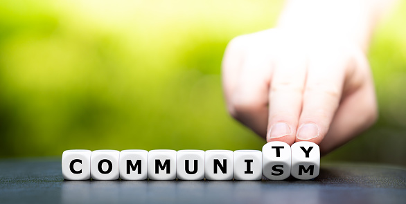 Hand turns dice and changes the word communism to community.