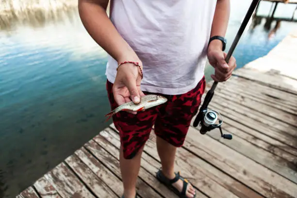 September 19, 2020 - Druskininkai, Lithuania: teenage boy standing on a lake jetty, holding, showing small fish catch with a fishing rod, summer vacation, close up