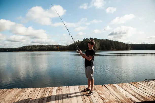 September 19, 2020 - Druskininkai, Lithuania: Teenage boy standing ready to start fishing with a fishing rod. Wooden jetty on a calm lake, healthy living.