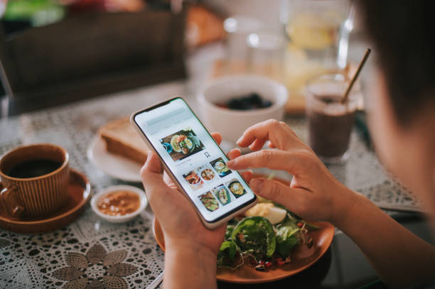 vista ad alto angolo mano della donna cinese asiatica sull'app mobile per la consegna di cibo online durante l'orario di colazione - ordinare foto e immagini stock