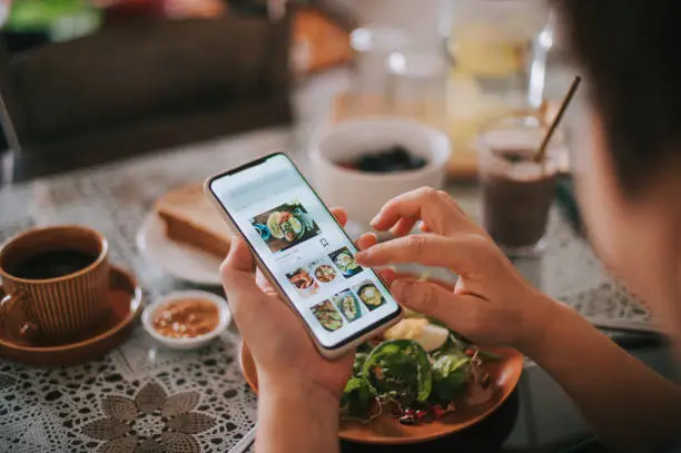 Photo of high angle view asian chinese woman's hand on mobile app for online   food delivery during breakfast time