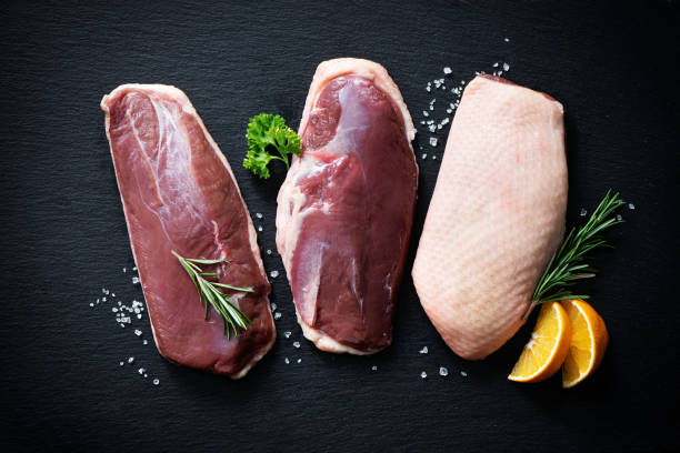 Raw duck breast pieces on dark slate background