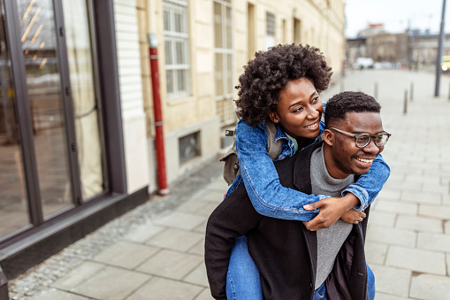 Happy afro couple in love walking in autumn city street. Woman hugging man from back