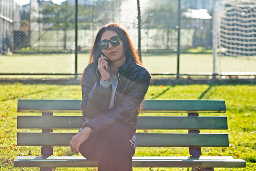 Young, beautiful, woman sitting on a bench in a public park using mobile phone