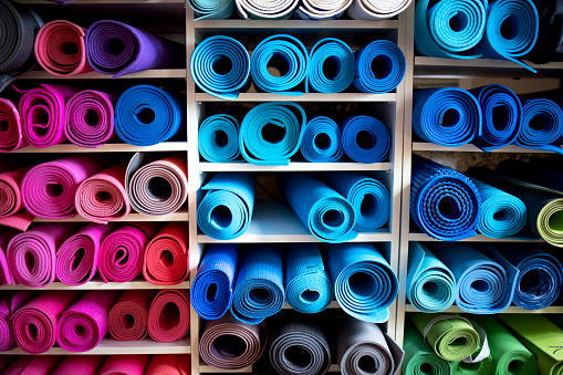 Yoga mats of many colors lying rolled up on shelves in gym repository