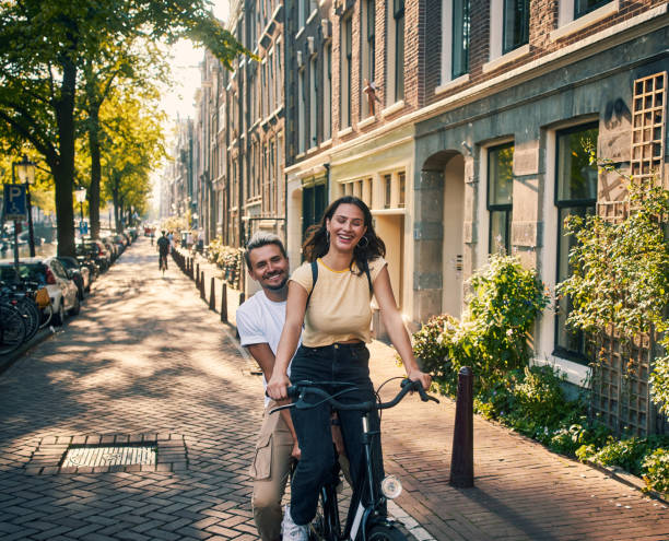 Netherlands, here we come! Shot of a young couple exploring the city of Amsterdam by bike netherlands stock pictures, royalty-free photos & images