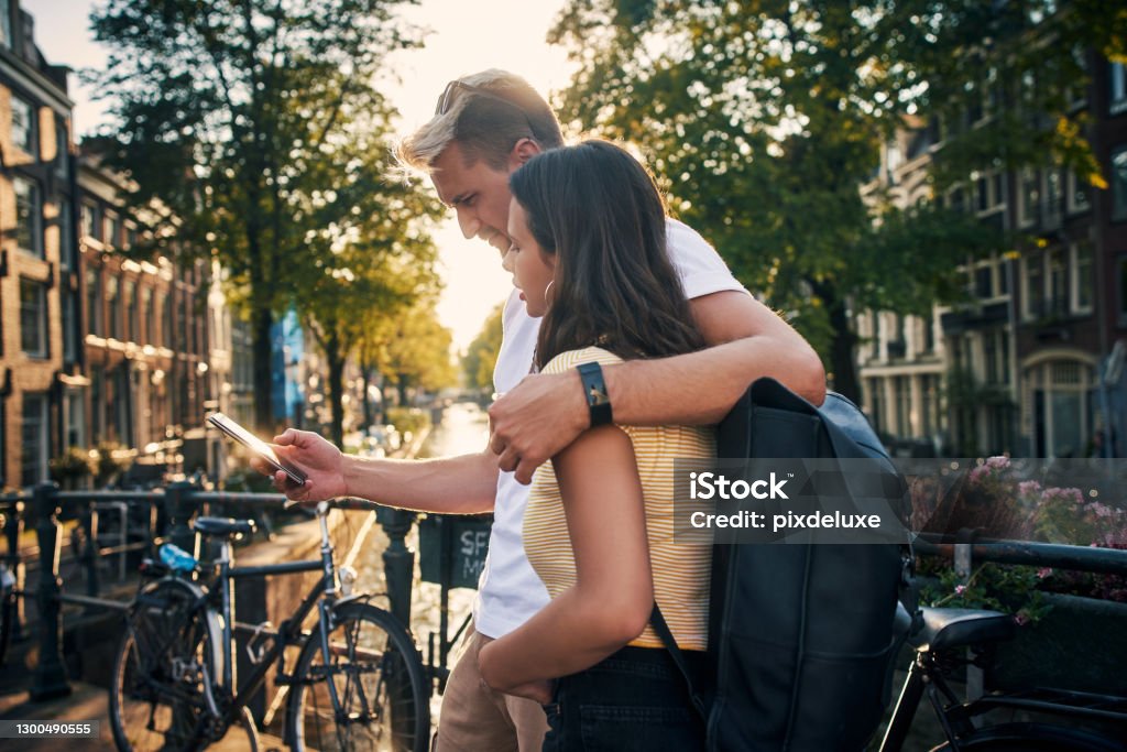 Why travel alone when you can travel with love Shot of a young couple using a smartphone while exploring the city of Amsterdam Couple - Relationship Stock Photo