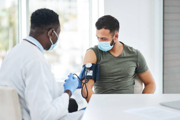 The sooner you know the sooner you can get treated Shot of a doctor examining a young man with a blood pressure gauge hypertensive photos stock pictures, royalty-free photos & images