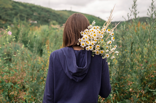 Rear view of young woman holding bouquet of daisies on her shoulder