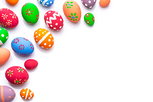 Overhead view of hand painted colorful Easter eggs arranged at the left of a white background leaving useful copy space for text and/or logo. High resolution 42Mp studio digital capture taken with Sony A7rII and Sony FE 90mm f2.8 macro G OSS lens