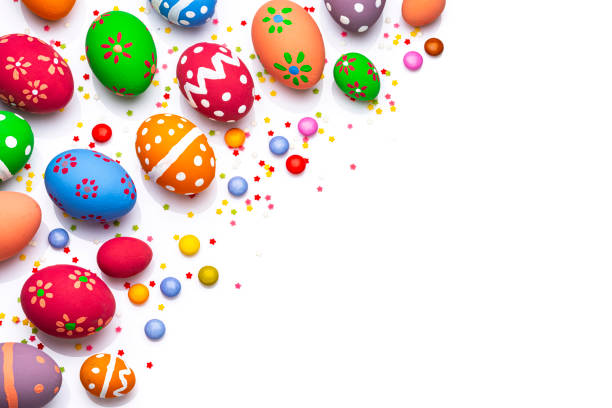 Overhead view of hand painted colorful Easter eggs arranged at the left of a white background leaving useful copy space for text and/or logo. Sugar sprinkles and candies complete the composition. High resolution 42Mp studio digital capture taken with Sony A7rII and Sony FE 90mm f2.8 macro G OSS lens