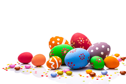 Group of hand painted colorful Easter eggs arranged at the bottom of a white background leaving useful copy space for text and/or logo. Sugar sprinkles and candies complete the composition. High resolution 42Mp studio digital capture taken with Sony A7rII and Sony FE 90mm f2.8 macro G OSS lens