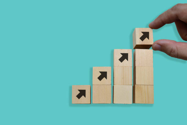 istock Close up Man hand arranging wood block stacking as step stair on blue background, copy space. 1300505814