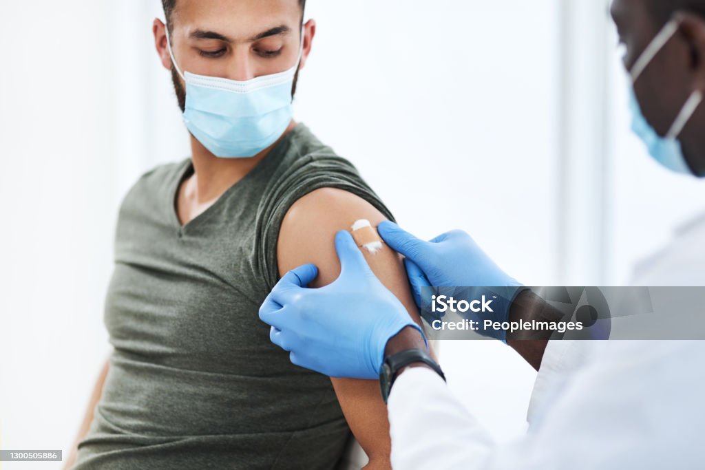 Gearing up for a global scale vaccination Shot of a doctor applying a band aid after injecting a patient in his arm during a consultation at a clinic Vaccination Stock Photo