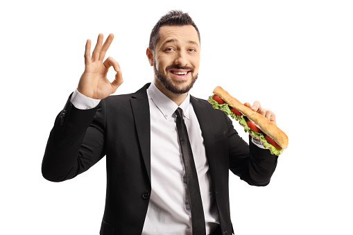 Businessman holding a sandwich in a baguette and gesturing ok sign isolated on white background