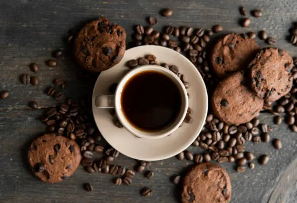 Photo of Coffee cup with cookies on wooden table background. Mug of black coffee with scattered coffee beans and cookies on a wooden table. Fresh coffee beans.