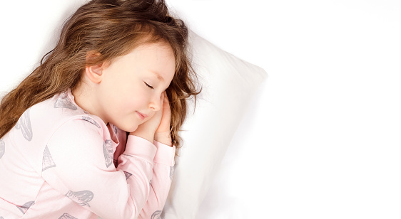 little beautiful girl with red hair in pink pajamas sleeping sweetly on a white pillow on a white background