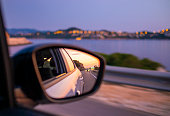 Traveling by car along beautiful coast at night. Reflection of sunset at side mirror.