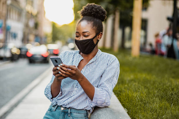 istock African American woman with mask is using mobile pjone 1300507557