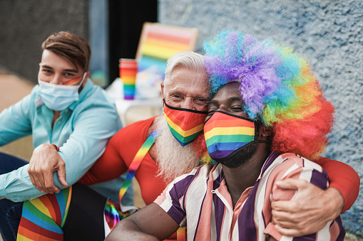 Multiracial gay men at lgbt pride event taking a selfie together while wearing protective face mask for coronavirus outbreak - Young and senior men