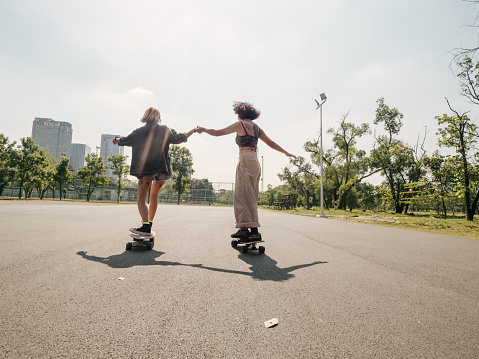 Two asian girls playing skateboard, happiness and enjoying at public park on holiday.