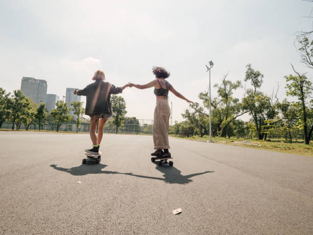 Young girls with riding longboard with friends Two asian girls playing skateboard, happiness and enjoying at public park on holiday. longboard skating photos stock pictures, royalty-free photos & images