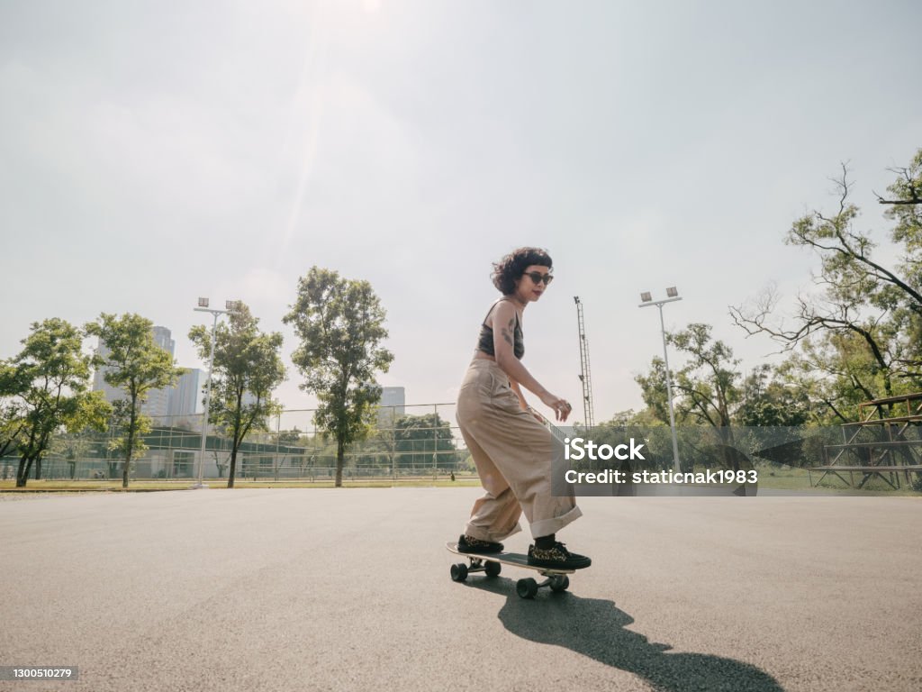 Teenage girl with skateboard in the park on a sunny day. Happy teenage girl driving skateboard at park in the city on a sunny summer day. Skateboarding Stock Photo