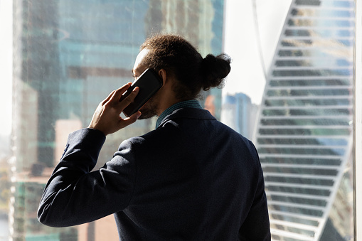 Back view of serious successful ethnic businessman in formalwear hold cellphone talk with business partner. Concentrated male employee or worker have smartphone call use mobile provider connection.