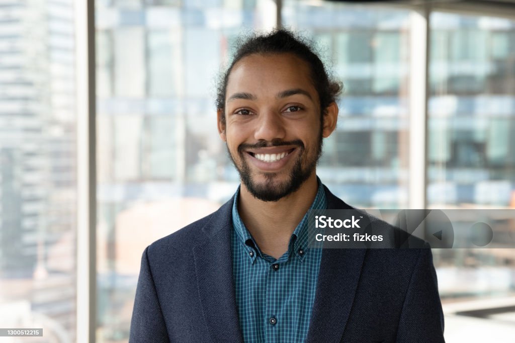 Headshot portrait of smiling ethnic businessman in office Headshot portrait of smiling young African American businessman in suit pose in own modern office. Profile picture of happy successful male boss or CEO in formalwear show confidence and leadership. Profile View Stock Photo
