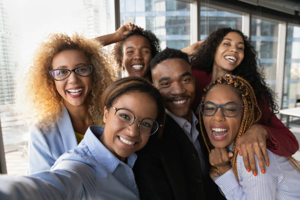 Portrait of smiling diverse colleagues pose for selfie Close up portrait of overjoyed young multiracial employees team have fun posing for selfie on smartphone in office together. Happy smiling diverse multiethnic colleagues male self-portrait picture. person of color stock pictures, royalty-free photos & images