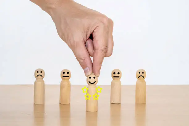 Photo of Close-up hand of a businessman choosing smiley face on wood doll, best excellent business services rating customer experience. Satisfaction survey concept, Star Satisfaction.