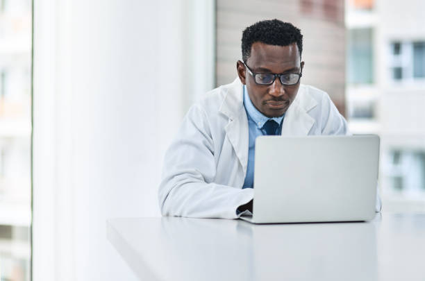 Doctors tools get more advanced by the day Shot of a young doctor using a laptop at his desk physician computer stock pictures, royalty-free photos & images