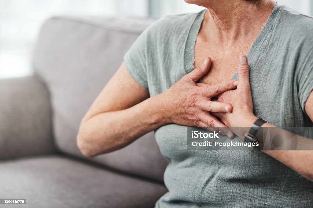 Guard your heart Shot of a senior woman suffering from chest pain while sitting on the sofa at home Heart - Internal Organ Stock Photo