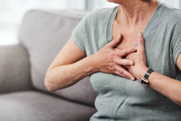 Guard your heart Shot of a senior woman suffering from chest pain while sitting on the sofa at home bronchitis stock pictures, royalty-free photos & images
