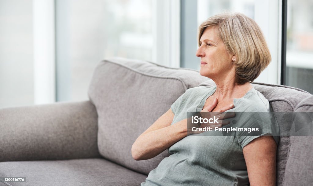 Chest pain is a cause for concern Shot of a senior woman suffering from chest pain while sitting on the sofa at home Heart Attack Stock Photo