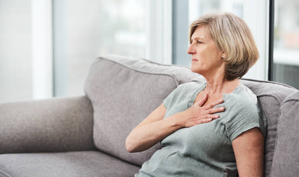 Chest pain is a cause for concern Shot of a senior woman suffering from chest pain while sitting on the sofa at home acute angle photos stock pictures, royalty-free photos & images