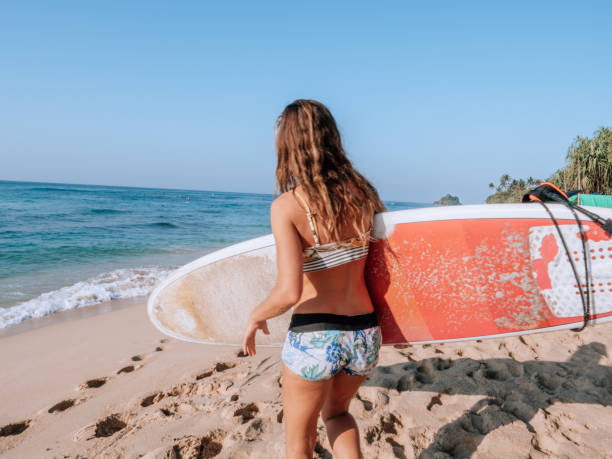 istock Woman on beach prepares for surfing 1300517512