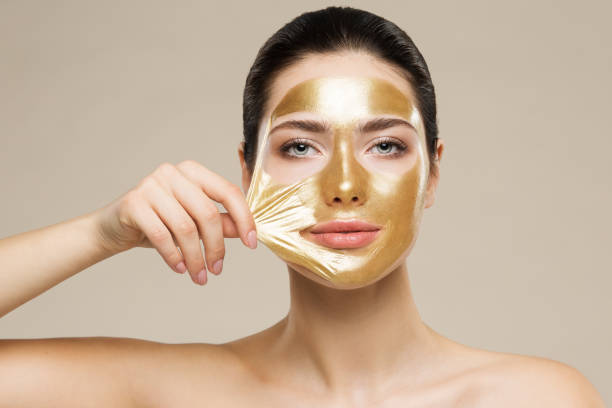 Woman peel off Gold Facial Mask. Collagen Golden Anti Aging Wrinkle Lifting Mask. Spa Beauty Treatment Woman peel off Gold Facial Mask. Collagen Golden Anti Aging Wrinkle Lifting Mask. Spa Beauty Treatment. Looking at camera. Beige Background facial mask beauty product stock pictures, royalty-free photos & images