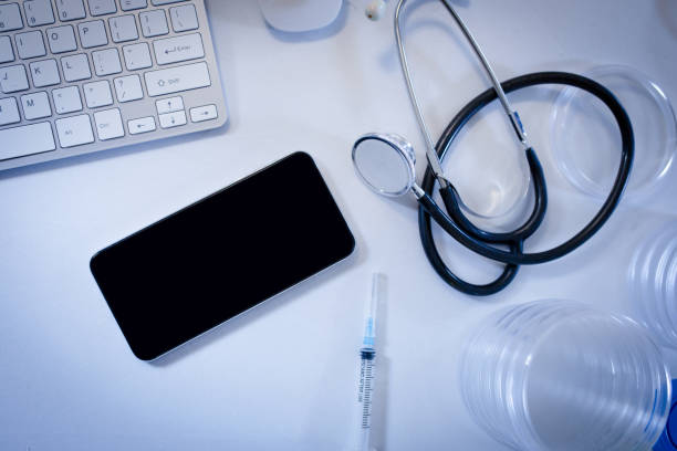 istock Desk in doctors surgery with smartphone computer keyboard syringe and stethoscope 1300520374