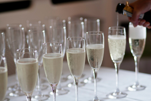 Champagne being poured in stylish glasses at luxury wedding reception/ celebration. Catering and service at feast on new year or Christmas celebrations.