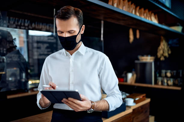 istock Waiter restaurant owner wearing mask using digital tablet 1300522081